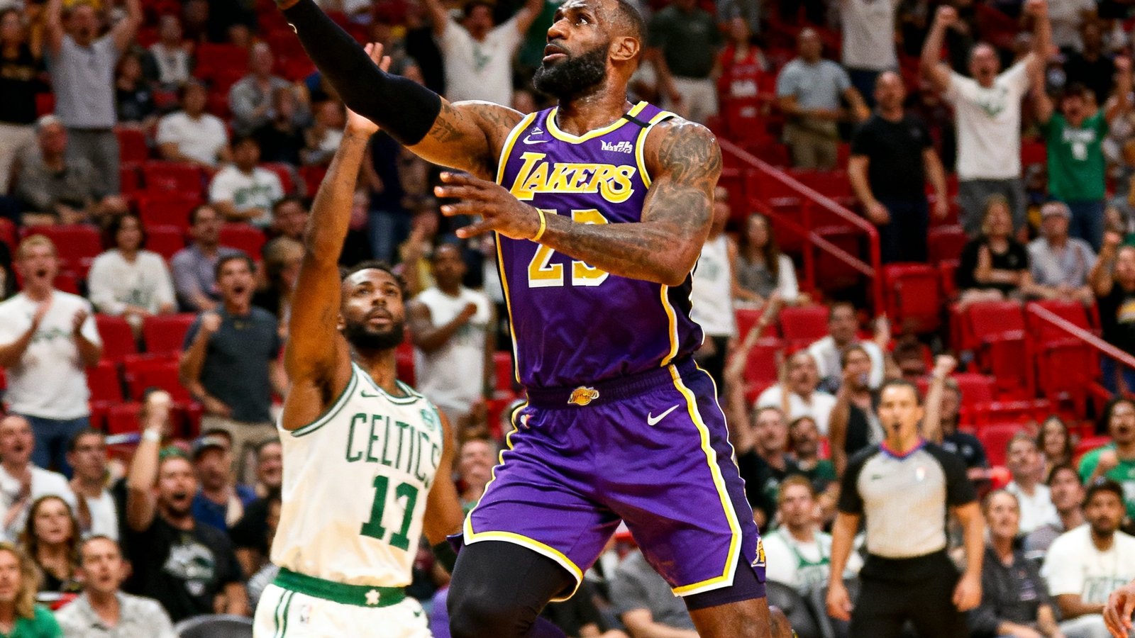 NBA常规赛湖人队主场比赛中，勒布朗·詹姆斯持球突破凯尔特人防守球员后飞身上篮的特写画面，球馆内观众纷纷起立欢呼。